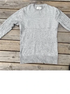 Grå stickad tröja från Emilio - Säljer en stilren grå stickad tröja från Emilio i storlek S. Tröjan har rund halsringning med ribbade detaljer och långa ärmar. Perfekt för dig som gillar enkel och klassisk design med mjukt material.