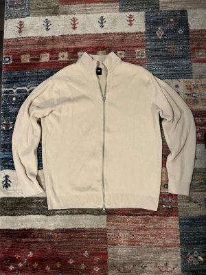 Beige kofta från ONLY & SONS - Säljer en stilren beige kofta från ONLY & SONS i ribbstickad bomull. Koftan har hel dragkedja framtill, hög krage och långärmad passform. Perfekt för lager-på-lager och funkar året runt. Snygg och enkel att matcha med det mesta.