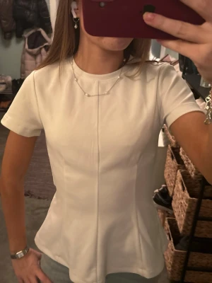 Vit figursydd topp från H&M - Säljer en stilren vit topp från H&M i storlek XXS. Toppen har korta ärmar och en figurnära passform med markerade sömmar framtill som ger en snygg siluett. Perfekt att matcha med jeans eller kjol för en clean look.känns som xs