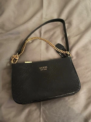 Väska, Guess - Svart handväska från GUESS, guldfärgade detaljer och kedja. Väskan är aldrig använd, dvs i nyskick. Skriv för fler bilder🩷
