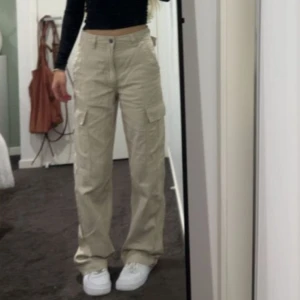 Beige cargopants  - Ett par beige cargobyxor flera stora fickor på sidorna. Byxorna har en avslappnad passform och är tillverkade i bomull. 