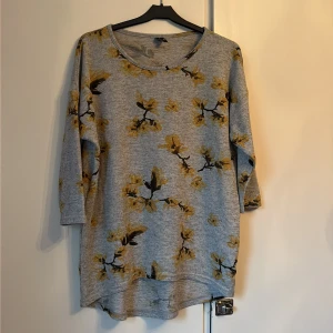 Grå blommig topp från Vero Moda - Säljer en grå topp från Vero Moda i storlek M med gult blommigt mönster. Toppen har rund halsringning och trekvartsärm. Materialet är mjukt och känns som bomull, perfekt för dig som gillar chill och snygga prints.