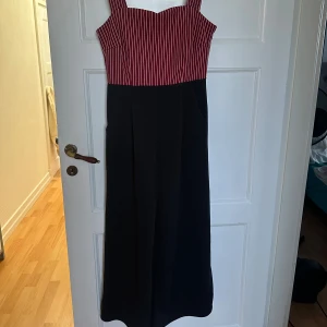 Randig jumper  med breda axelband - Snygg jumper med breda axelband och röd- och vitrandig överdel. Kjoldelen är helsvart och har en rak, elegant passform. Jumpern har en markerad midja och dragkedja i ryggen. Perfekt för dig som vill sticka ut med en cool och stilren look.