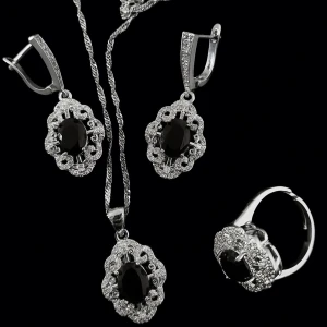 Smyckesett silverpläterad 925 - Elegant smyckeset med örhängen, halsband och ring i silverfärg. Alla delar har en stor svart oval sten i mitten, omgiven av glittrande stenar i en dekorativ ram. Perfekt för dig som gillar klassisk och lyxig stil. Justerbar ring