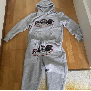 Grå mjukisbyxor Trapstar London Shooters - Säljer ett par grå mjukisbyxor från Trapstar med stort broderat London Shooters-motiv och svart panter på framsidan. Byxorna har snörning i midjan och ribbade muddar vid bensluten. Perfekt för chill och streetwear.