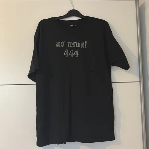 Svart t-shirt med strass och vingar Cropp - Svart oversized t-shirt från Cropp med coola strassdetaljer. Framsidan har texten 'as usual 444' i glittriga stenar och baksidan pryds av stora änglavingar i strass. Skön bomullskvalitet och loose fit för en avslappnad vibe.