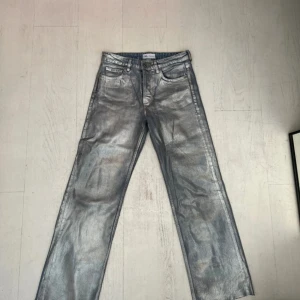 Silvriga raka jeans från Zara - Unika jeans från Zara i metallic silver med rak passform och klassisk femficksdesign. Jeansen har normal midja och är tillverkade i ett jeansmaterial med glansig finish som verkligen sticker ut. De är aningens klippta nedtill