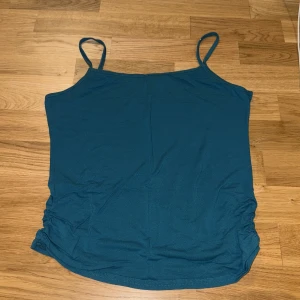 Vintage Turkos linnetopp med rynkade sidor - Säljer en vintage turkos linnetopp med smala axelband och snygga rynkade detaljer på sidorna. Toppen har en enkel och stilren design, perfekt för varma dagar. Materialet känns mjukt och lätt mot huden.