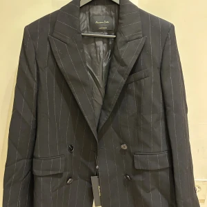  Ny med prislapp Randig svart kavaj från Massimo Dutti - Snygg svart kavaj från Massimo Dutti med tunna vita ränder. Klassisk dubbelknäppt modell med breda slag, fickor med lock och knappar vid ärmslut. Perfekt för en stilren look. Tillverkad i Portugal.