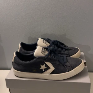 Mörkblåa Converse Cons  - Säljer ett par Converse Cons sneakers i mörkblå mocka med vita detaljer och snörning. Klassisk låg modell med vit sula och Converse-logga på sidan och plösen. Perfekta för dig som vill öka din stil och vill ha något som sticker ut lite extra.