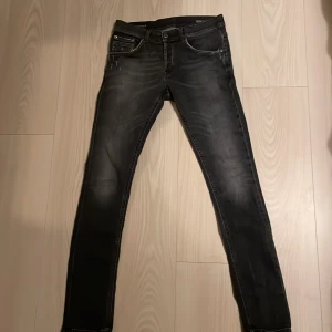 Svarta skinny jeans från Dondup - Snygga svarta jeans från Dundup med skinny passform och klassisk femficksdesign. Jeansen har slitna detaljer framtill, silverfärgade nitar och en liten D-logga på bakfickan. Materialet är stretchigt denim som sitter tajt och bekvämt.