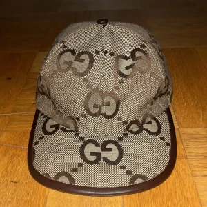 Gucci keps  - Säljer en snygg keps från Gucci i beige och brunt med det klassiska GG-monogrammet över hela kepsen. Kepsen har böjd skärm med brun kant och är tillverkad i bomullsmix. Perfekt för dig som vill sticka ut med en lyxig accessoar.
