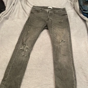 Grå ripped jeans från Zara Man - Säljer ett par grå jeans från Zara Man Denimwear med snygga slitningar och ripped detaljer på benen. Modellen har klassisk femficksdesign, raka ben och normal passform. Jeansen är tillverkade i denim och har en cool, lite tvättad look.