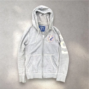 Grå hoodie från American Eagle - Säljer en denna sjukt ovanliga och galet snygga american eagle zip-hoodien. Storlek S sitter true to size och passar bäst på folk ~170-183~ (jag på bilden är 177 runt 63-64 kg för referens. Pris: 549 (kan sänkas vid snabb affär) (OBS: finns ett litet hål vid dragkedjan men påverkar knappt) Skickar inom 24 timmar 🙌hör gärna av er vid frågor! Kolla även gärna in vår profil om du är sugen på mer liknande vintagekläder från märken som Hollister, American Eagle, Abercrombie osv. MVH Love! 