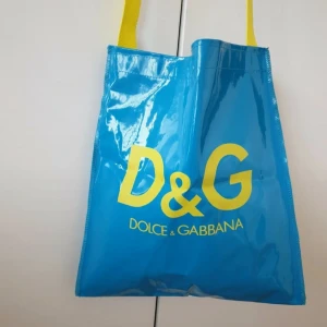 Dolce & Gabbana vintage väska  - Cool blå shoppingväska från Dolce & Gabbana med stora gula D&G-bokstäver och matchande gula axelband. Väskan har en glansig finish och är tillverkad i syntetmaterial, perfekt för att bära med sig allt man behöver. Snygg och färgstark accessoar för dig som gillar statement pieces.Oanvänd äkta  vintage dolce gabbana  väska, defekt kan förekomma, ny pris 1000