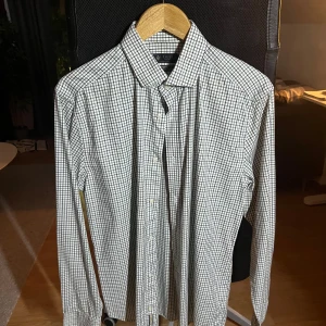 Rutig skjorta från Riley slim fit - Snygg rutig skjorta från Riley i slim fit-modell. Skjortan har ett klassiskt krage, knappar framtill och långa ärmar. Mönstret är grönt och blått på vit botten, vilket ger en fräsch och stilren look. Perfekt för dig som gillar en clean och modern stil.