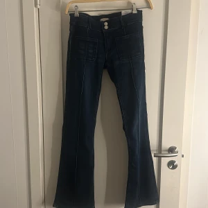 Mörkblå bootcut jeans från Gina Tricot - Snygga mörkblå jeans från Gina Tricot med bootcut passform och höga fickor framtill. Jeansen har två knappar i midjan och markerade sömmar längs benen.