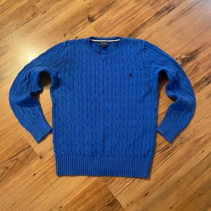 Blå kabelstickad tröja Polo Ralph Lauren - Kabelstickad blå tröja från Polo Ralph Lauren med rund halsringning och klassisk broderad logga på bröstet. Tröjan har ribbade muddar och nederkant, samt långärmad passform. Sitter som size S/170 och längden är 60 cm, bredden 43 cm och ärmlängden 56 cm. I mycket bra skick utan defekter.                         Hör av er om ni har frågor 🤩