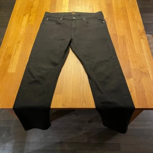 Svarta jeans från Lee - Svarta jeans från Lee med raka ben. Jeansen har Lee-logga på bakfickan och är tillverkade i ett mjukt bomullstyg med lite stretch. Perfekta för dig som gillar en modern och stilren byxa