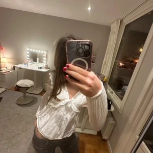 Vit volangblus från Gina Tricot - Supersöt vit blus från Gina Tricot med v-ringning, volangdetaljer och långa ärmar. Perfekt att styla med jeans eller kjol för en söt outfit 💓 säljer för att jag inte tycker den passar mig längre. (är lite liten i storlek men funkar oxå som 146/152)