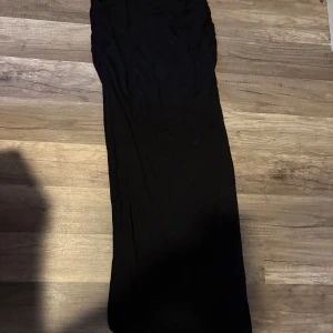 Svart långkjol i mjukt tyg - Säljer en svart långkjol med rak passform. Kjolen är enkel och stilren, perfekt för dig som gillar minimalistisk look. Materialet känns mjukt och följsamt mot huden. Passar dig som vill ha en klassisk svart kjol med lite extra längd. 