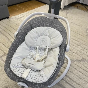  2-in-1 Baby Swing - Joie Sansa 2-in-1 babysitter och gunga i grått och vitt mönster. Elektronisk styrpanel med flera funktioner, säkerhetssele och mjuk  , Perfekt för småbarn med komfort och säkerhet.