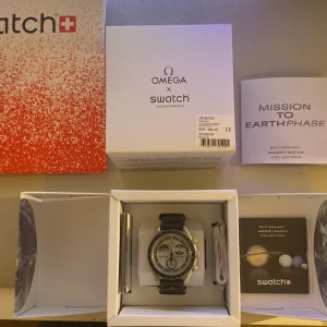 Omega x Swatch MoonSwatch Earthphase - Säljer en Omega x Swatch MoonSwatch Mission to Earthphase. Klockan har en rund urtavla i silver och svart med unika månfasdetaljer och tachymeter. Boetten är i biokeramik och bandet är svart med Omega-logga. Kommer komplett med originalbox och manualer.
