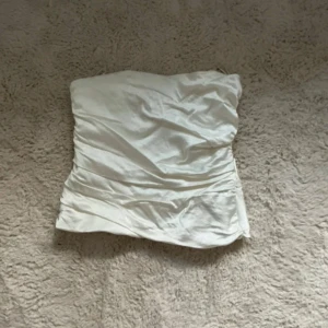 Vit bandeau topp Zara - Säljer en snygg vit bandeau tubtopp från Zara i storlek S. Toppen har en stilren och slät design med lätt rynkade detaljer och dragkedja baktill. Materialet känns mjukt och har en satinlik finish som ger en lyxig vibe. Perfekt för att skapa en clean och trendig look. Köp direkt för 149kr!!😍😍💞