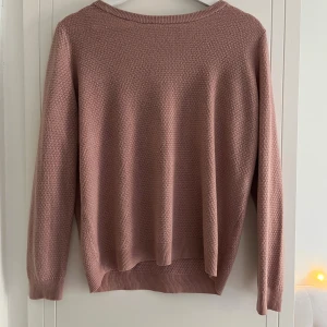 Rosa stickad tröja med struktur - Mysig rosa stickad tröja med diskret strukturmönster. Tröjan har rund halsringning, långa ärmar och ribbade muddar vid ärmslut och nedertill. Tunnare material. Mjukt material. 