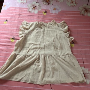 Beige volangklänning från Grawell - Söt kortklänning från Grawell i beige med diskret prickigt mönster. Vi köpte från shein. Klänningen har volangdetaljer vid axlarna och halsen, är ärmlös och har en lätt A-linjeformad siluett. Tillverkad i mjuk polyester som känns skön mot huden.