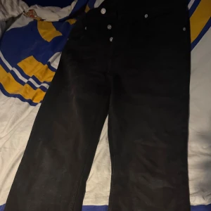 Svarta straight jeans från Levi's - Säljer ett par svarta jeans från Levi's med klassisk straight fit och silverfärgade knappar. Byxorna har fem fickor och en enkel, tidlös look som funkar till det mesta. Perfekt för dig som gillar en clean och stilren vibe.