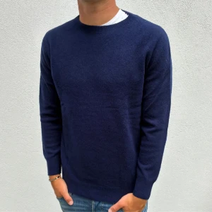 Mörkblå stickad tröja herr - Snygg mörkblå stickad tröja med rund hals och långa ärmar. Perfekt för dig som gillar en enkel och stilren look. Tröjan har ribbade muddar vid ärmslut och nederkant, och passar bra till jeans.