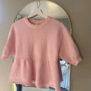 Ljusrosa stickad topp från nelly - Superfin ljusrosa stickad topp från nelly i storlek XS. Modellen har korta ärmar, rund hals och en volangliknande söm nedtill som ger en söt och avslappnad vibe. Perfekt för dig som gillar mjuka material och pastellfärger.