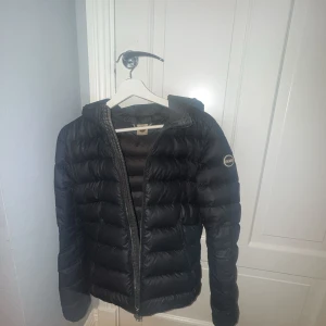 Svart Colmar dunjacka med luva - TRYCK INTE PÅ KÖP DIREKT Svart dunjacka från Colmar med luva och dragkedja framtill. Jackan har ett puffigt quiltat mönster och Colmar-logga på ärmen. Perfekt för kalla dagar och har en stilren look som funkar till det mesta. Jackan är i st 42, och passar mig som vanligtvis andvönder s-xs. Om du har några frågor så är det ba att fråga. 