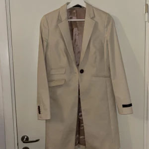 Beige kavaj från Morris Lady - Stilren beige kavaj från Morris Lady med klassisk passform och snyggt satin-foder. Kavajen har en knapp framtill, fickdetaljer och knappar vid ärmslut. Perfekt för dig som gillar en tidlös och clean look.