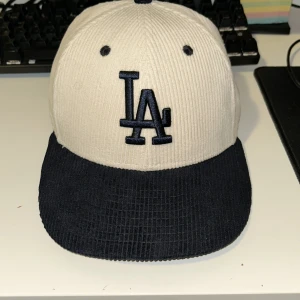 LA Dodgers keps i manchester från New Era - Snygg och Unik! LA Dodgers keps från New Era i 59FIFTY-modell. Kepsen är gjord i ribbad manchester med beige krona och mörkblå skärm. Broderad LA-logga framtill och MLB-logga bak. Perfekt för dig som gillar streetwear och sportig stil. 