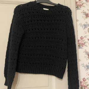Svart stickad tröja från H&M - Svart stickad tröja från H&M med hålmönster och ribbade muddar vid hals, ärmslut och nederkant. Tröjan har lång ärm och en lite loose passform. 