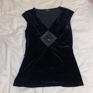 Svart sammetsblus med paljettdetalj - Säljer en svart blus från Jonden i sammet med v-ringning och en stor fyrkantig paljettdetalj framtill. Blusen är ärmlös och har lätt rynkade axlar som ger en cool siluett. Perfekt för dig som gillar att sticka ut med glansiga detaljer!💕🌸