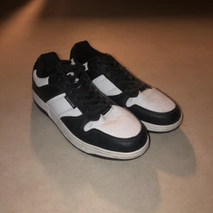 Svarta och vita sneakers Jack & Jones - Snygga sneakers från Jack & Jones i svart och vitt med klassisk låg profil. Skorna har snörning, rund tå och platt sula. Ovandelen är i syntetmaterial med kontrasterande paneler och märkets logga på sidan och hälen. Perfekta för en streetinspirerad look.   ANVÄND 2 GÅNGER