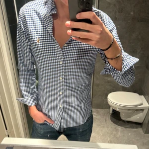 Rutig blåvit skjorta från Ralph Lauren - Snygg rutig skjorta från Ralph Lauren i blått och vitt med klassisk krage och knappar framtill.  Skjortan är i riktigt bra skick. Jag på bilden är 188cm. Hör av er vid funderingar;)