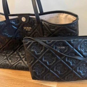Svart quiltad shoppingväska från Guess - Säljer en svart quiltad shoppingväska från Guess med matchande mindre väska. Väskorna har Guess-logga i guld, snyggt mönstrad utsida och långa handtag. Tillverkad i syntetmaterial med ljus insida och tryckt Guess-mönster. Perfekt för dig som gillar stilrena accessoarer.