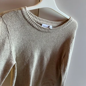 Beige stickad tröja från Vila - Mysig beige stickad tröja från Vila med rund halsringning och ribbade muddar. Perfekt för lager-på-lager och enkel att matcha med jeans eller kjol. 