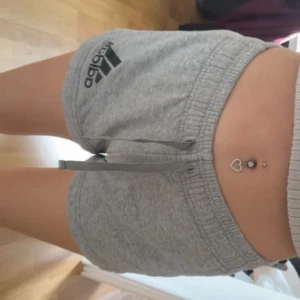 Grå Adidas shorts med snörning - Snygga grå shorts från Adidas med klassisk logga på vänster sida. De har elastisk midja och snörning framtill för skön passform. Perfekta för träning eller chill hemma. Mjukt material som känns bekvämt mot huden.