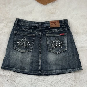 Jeanskjol med kronbrodyr Seyoo Jeans - Cool mörkgrå jeanskjol från Seyoo Jeans med snygga slitningar och broderade kronor med pärldetaljer på fickorna. Står storlek L, men passar en xs/s mer (mindre i storlek) 💜midja: 74cm 