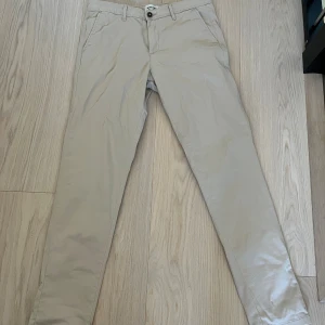Beige chinos från Jack & Jones slim - Snygga beige chinos från Jack & Jones i slim fit-modell. Byxorna har klassiska sidfickor, två bakfickor med dragkedja och bälteshällor. Perfekta för en clean och stilren look. Tillverkade i bomull för en skön känsla hela dagen.