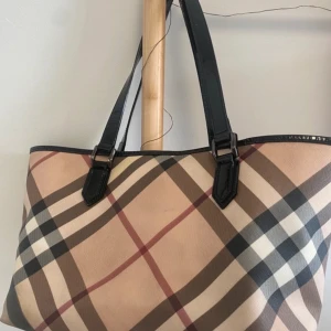 Burberry väska🌸 - Snygg axelväska från Burberry med klassiskt rutigt mönster i beige, svart, vitt och brunt. Väskan har svarta handtag och metallfötter undertill. Perfekt storlek för vardagens alla prylar och ger en lyxig touch till din outfit. Väskan är använd och defekter förekommer.🤍🌸