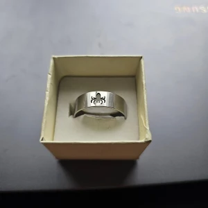 Silverfärgad ring med spindelmotiv - Cool bred ring i silverfärgad metall med ett utstansat spindelmotiv framtill. Perfekt för dig som gillar edgy detaljer och vill sticka ut med din stil. Rostfritt stål, 21 mm
