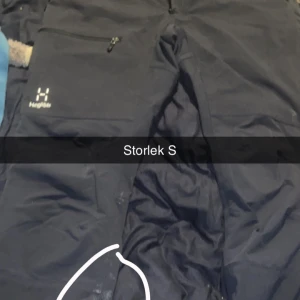 Svarta täckbyxor från Haglöfs S - Svarta täckbyxor från Haglöfs med dragkedjeficka på benet och diskret logga. Perfekta för kalla dagar och utomhusaktiviteter. Funktionellt material som står emot väder och vind. Har ett brännare men ingen hål där de ringat annars perfekta
