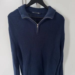 Marinblå stickad tröja med half zip - Snygg marinblå stickad tröja från 157 med grov struktur och krage. Tröjan har en half zip-dragkedja framtill och långa ärmar. Perfekt för dig som gillar en chill och stilren look under höst och vinter.