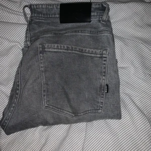 Grå jeans från BOSS - Snygga grå jeans från BOSS med klassisk femficksdesign och svarta detaljer vid midjan. Jeansen har en rak passform och är tillverkade i mjukt denimtyg. Perfekta för dig som gillar en stilren och avslappnad look.